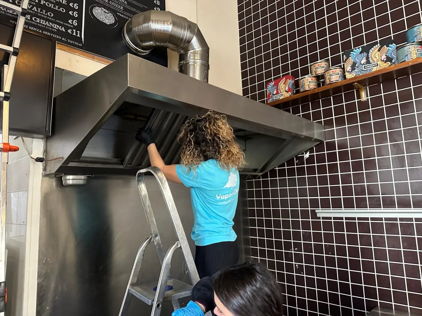 Operatrice VaporChic sgrassa la cappa aspirante in acciaio di una cucina professionale Operatrice VaporChic sgrassa la cappa aspirante in acciaio di una cucina professionale